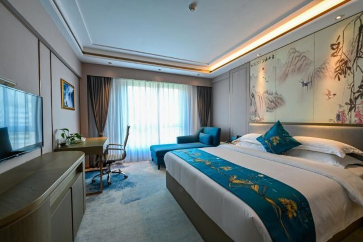 A hotel room with a large bed, a desk with a chair, a TV, and a painting on the wall.