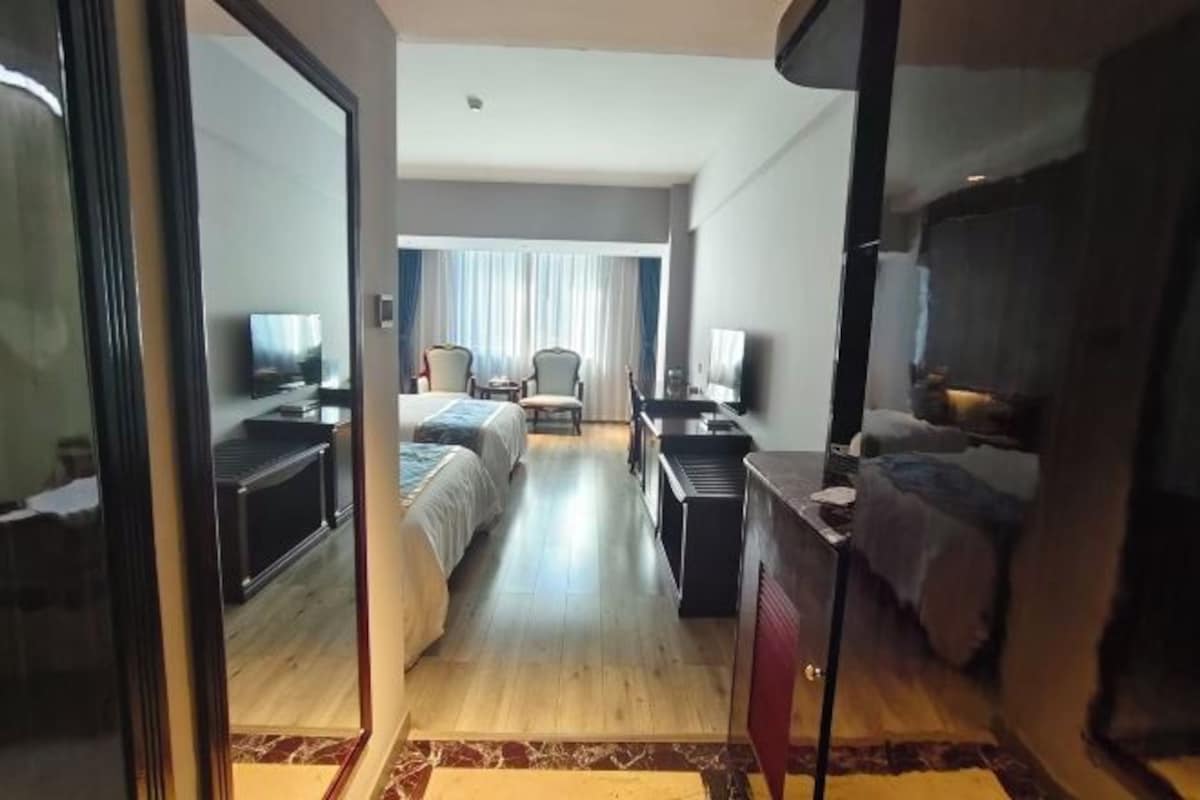 A hotel room with a bed, a desk, a chair, a TV, and a window with curtains.