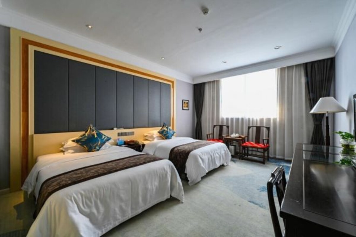 A hotel room with two beds, a desk, and a chair.
