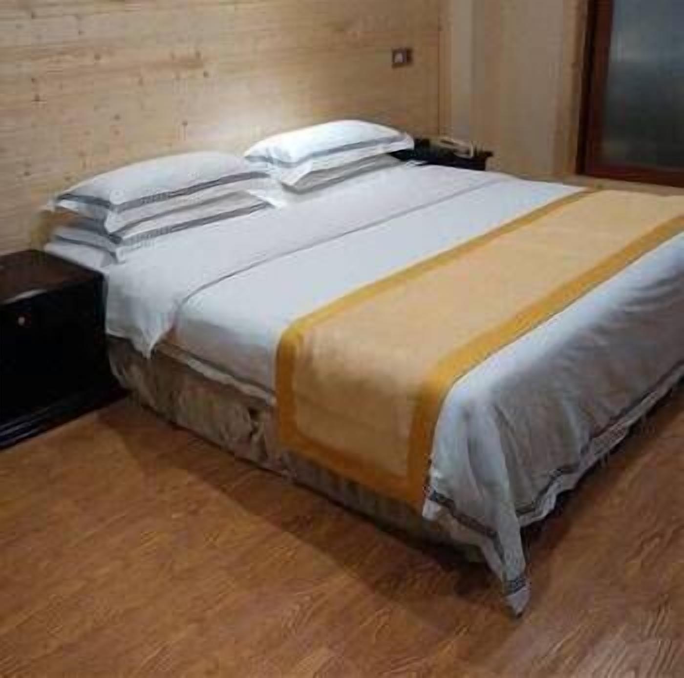 A single bed with a white and yellow bedspread, a wooden headboard, and a nightstand with a phone.