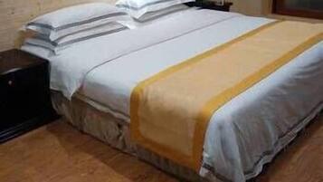 A single bed with a white and yellow bedspread, a wooden headboard, and a nightstand with a phone.