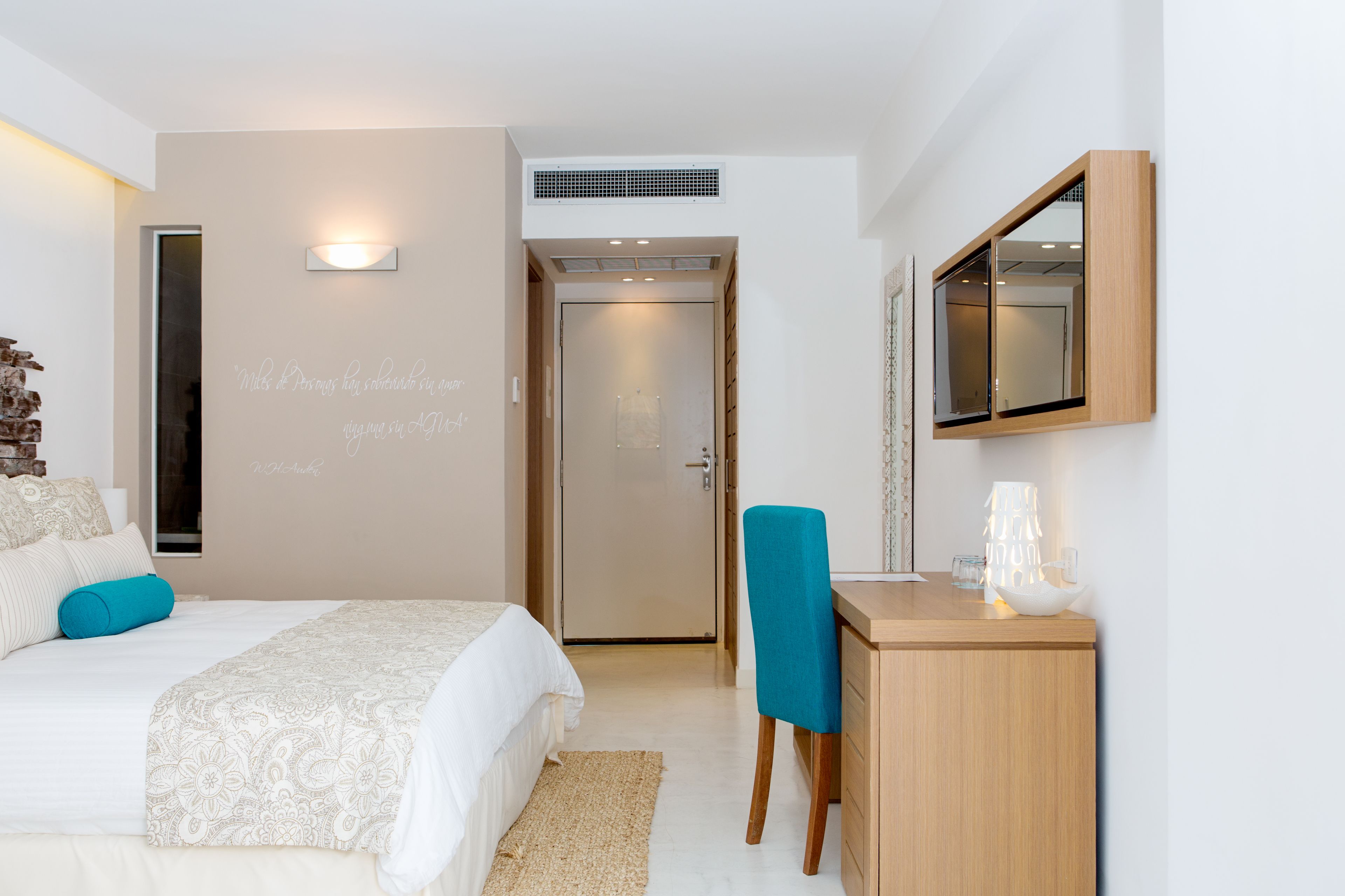 A bedroom with a bed, a desk, a mirror, and a door.