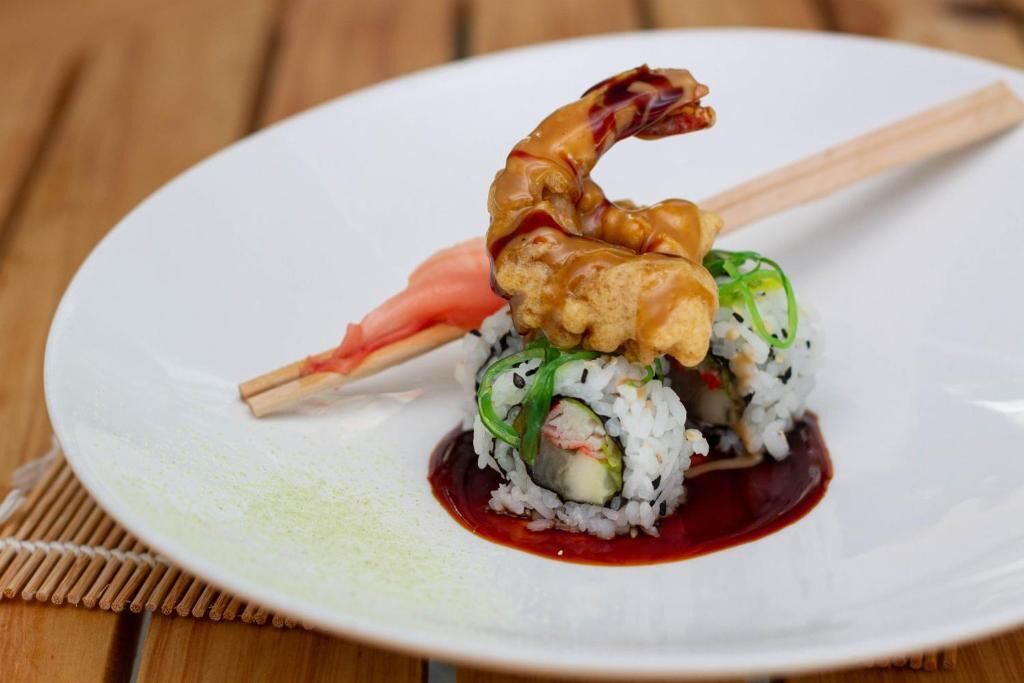 A plate of sushi with a dipping sauce and a pair of chopsticks.