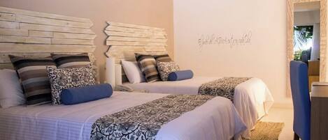Une chambre avec deux lits, chacun agrémenté de draps et d’oreillers à motifs, d’une tête de lit en bois, d’un mur orné d’une inscription décorative et d’un miroir.