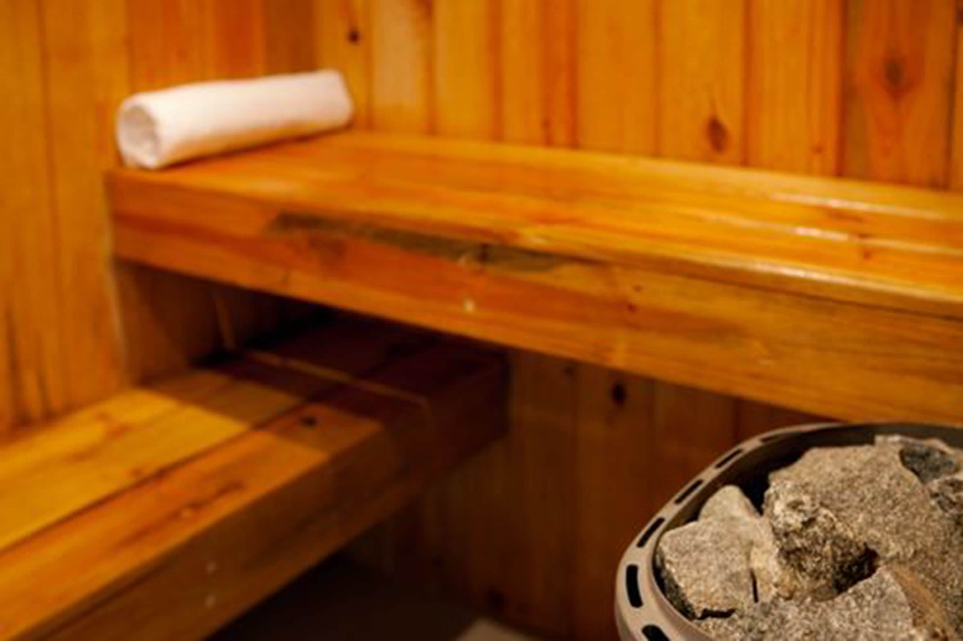 A wooden sauna bench with a towel and a basket of stones.