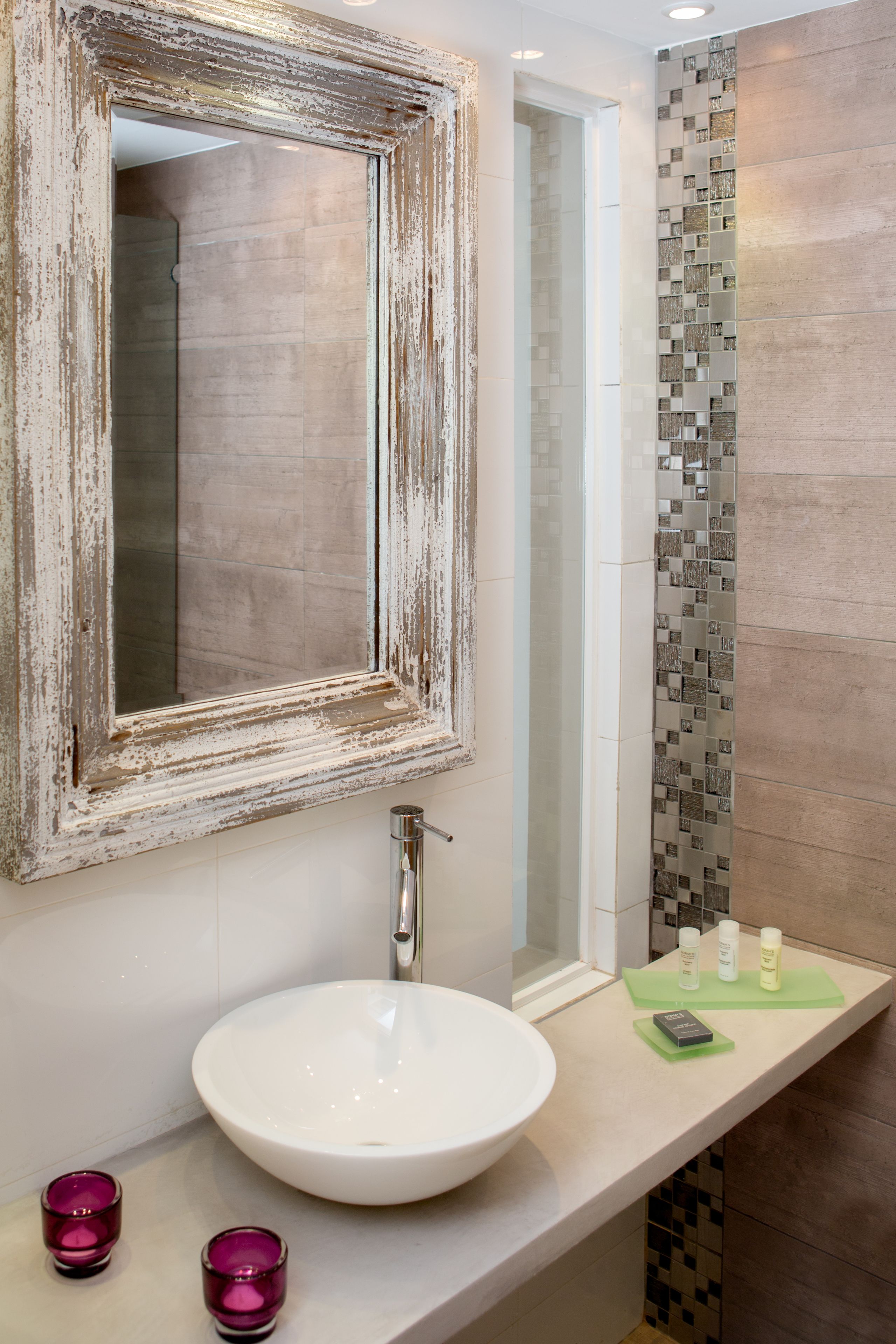A bathroom with a white sink, a mirror with a distressed frame, and a tiled shower area.