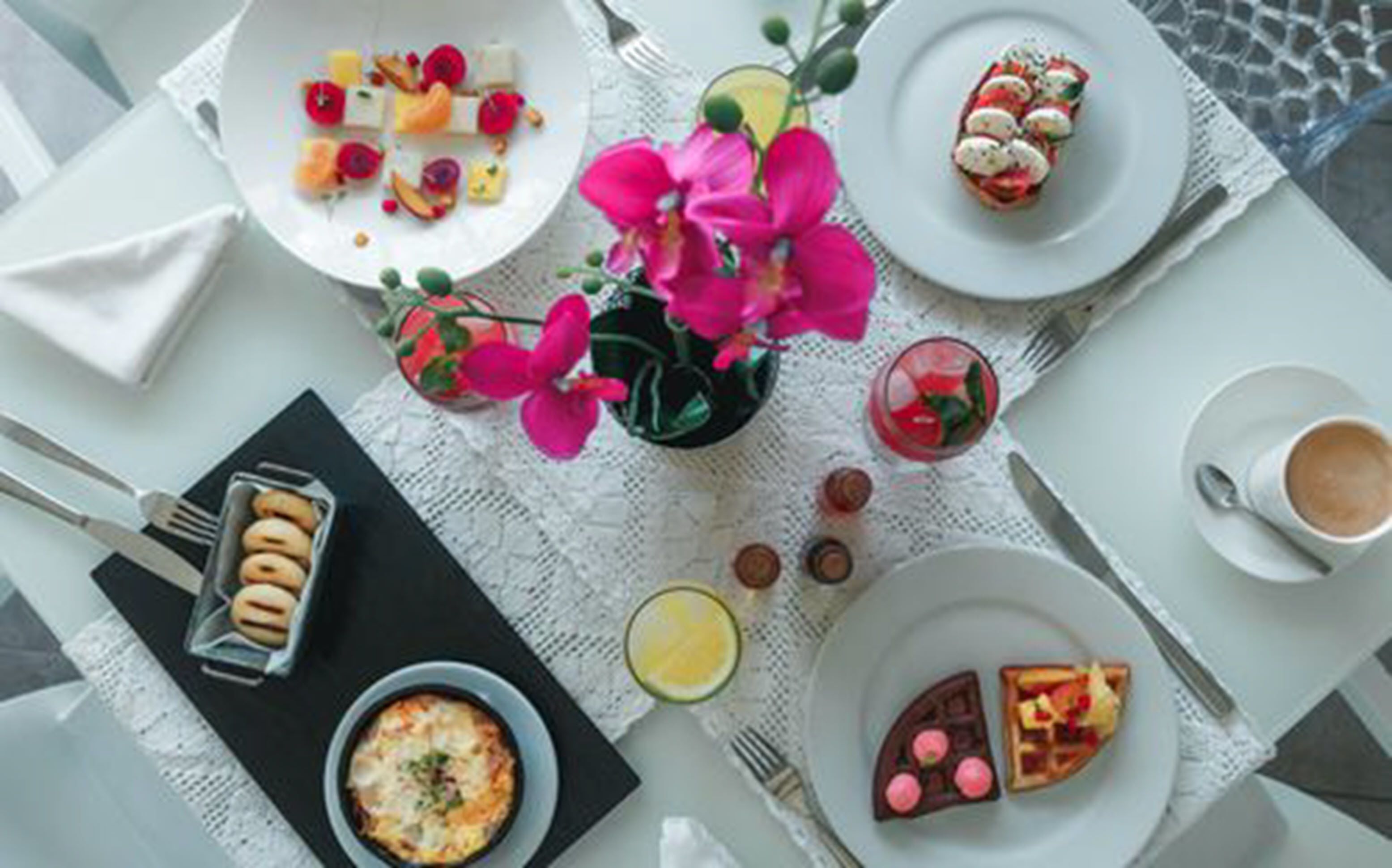 A table set with various dishes, including a dessert with pink flowers, a bowl of soup, and a plate with a chocolate dessert.