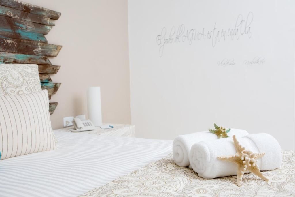 A neatly made bed with rolled white towels and a starfish decoration, a phone, and a wall with a decorative script.