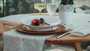 Una mesa de comedor con un plato de comida, dos copas de vino blanco y una orquídea en maceta.