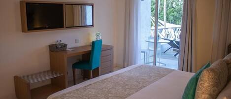 A hotel room with a bed, a desk with a chair, a small bench, a large window with a view of a balcony, and a mounted TV.