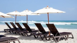 Una playa con filas de tumbonas y sombrillas blancas.