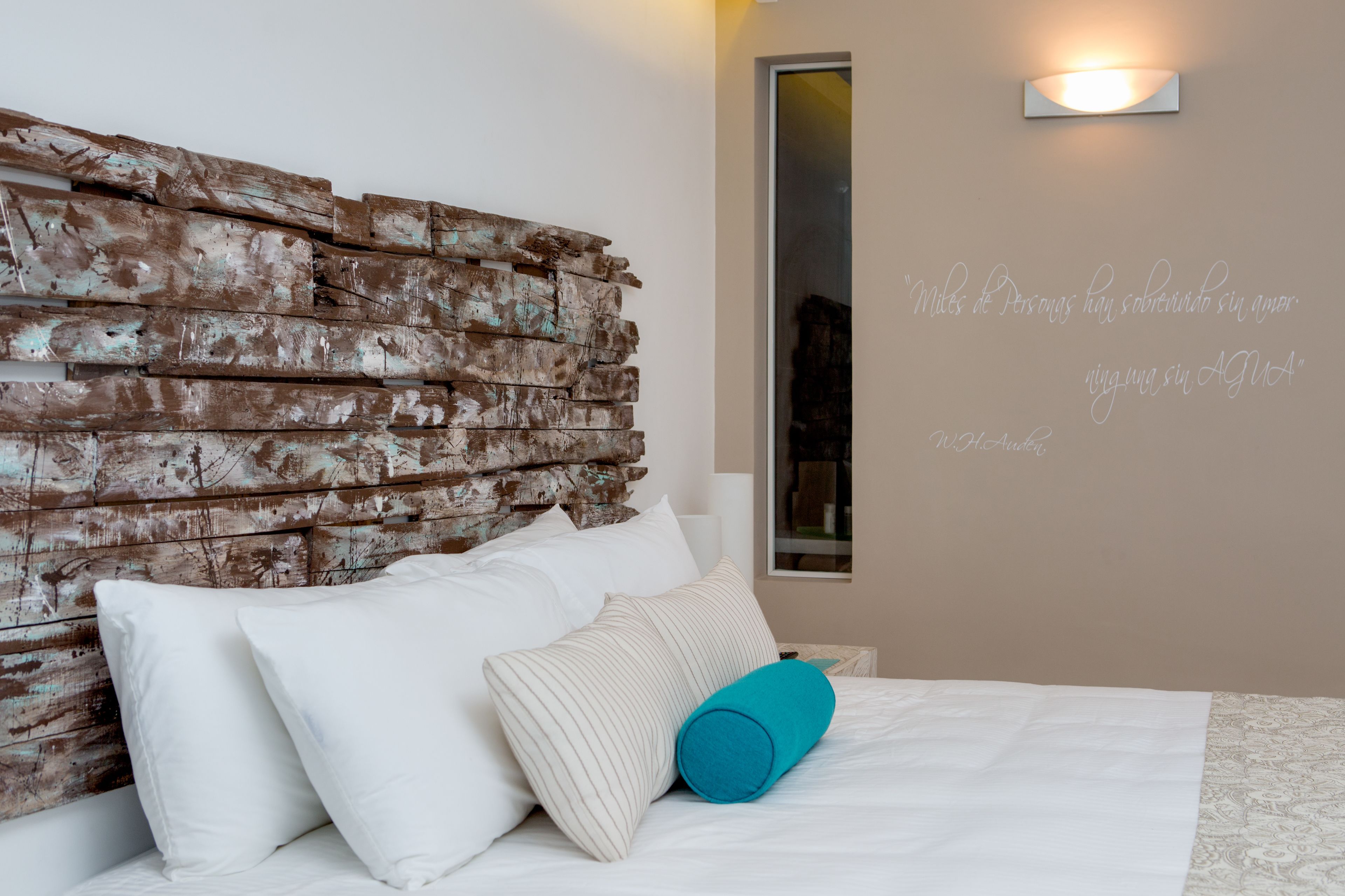 A bedroom with a rustic wooden headboard, white bedding, and a decorative pillow.