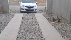 A pathway leading to a white car parked in a gravel area with concrete borders. - Casa Gobernador Gregores Patagonia (Gobernador Gregores)