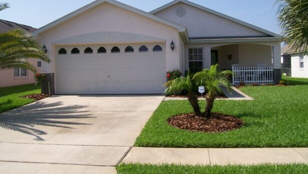 A single-story house with a garage, a covered porch, and a well-maintained lawn with a palm tree. - 4BR 3BA Home in Indian Creek by CV-2653 (Kissimmee)