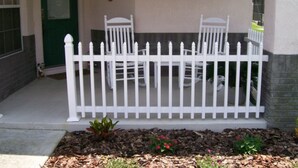 A white picket fence with two chairs behind it, a green door, and a small garden with mulch and plants. - 4BR 3BA Home in Indian Creek by CV-2653 (Kissimmee)