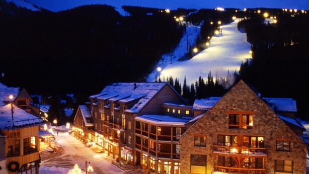 A snow-covered town with illuminated buildings and a ski slope in the background. - River Run Village 2 Bedroom Condo - 100 yards to slopes, Pool, Hot Tub Access (Keystone)