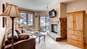 A cozy living room with a stone fireplace, a television mounted above it, and a wooden cabinet. - River Run Village 2 Bedroom Condo - 100 yards to slopes, Pool, Hot Tub Access (Keystone)