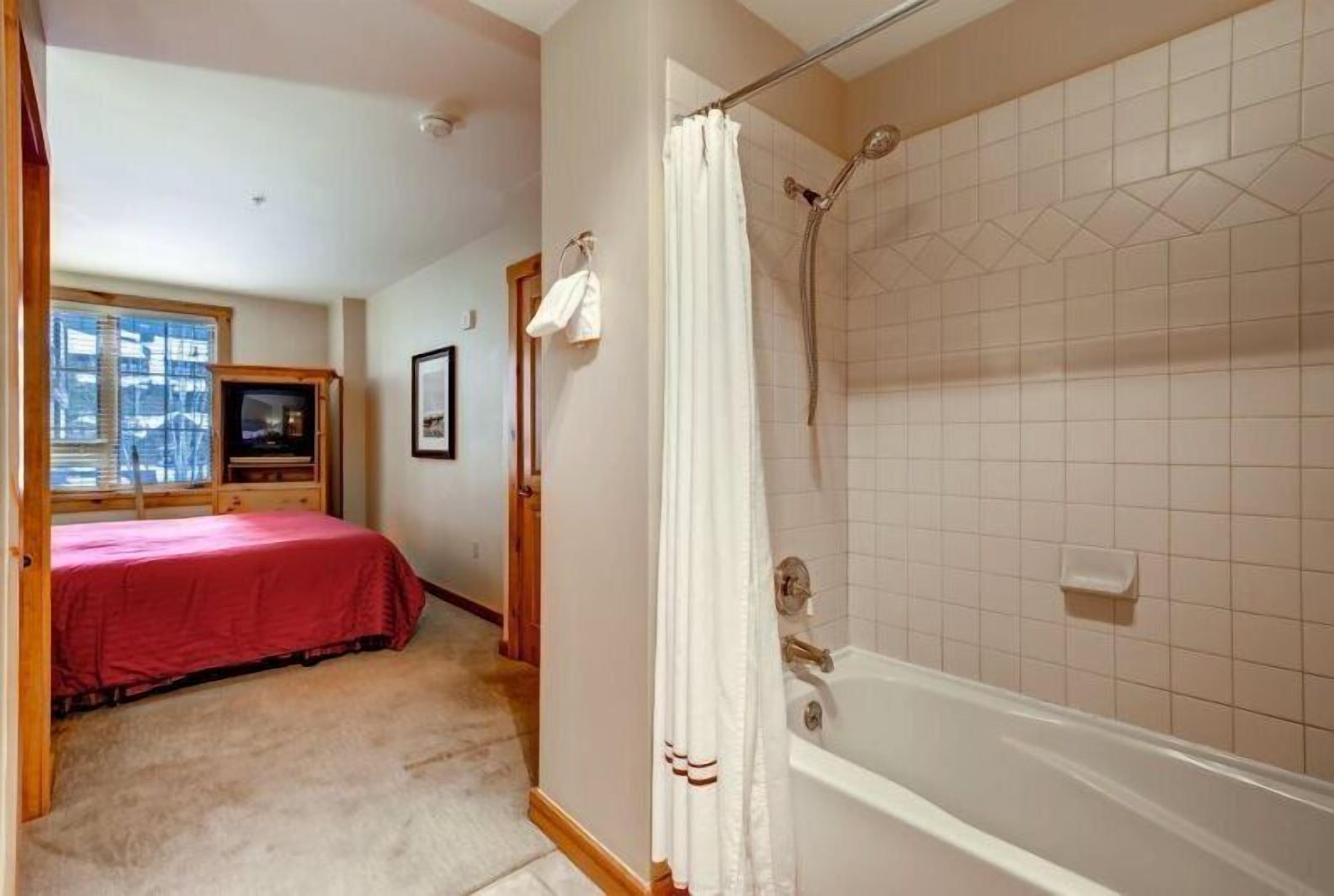 A bedroom with a red bedspread, a wooden headboard, a window, and a television.