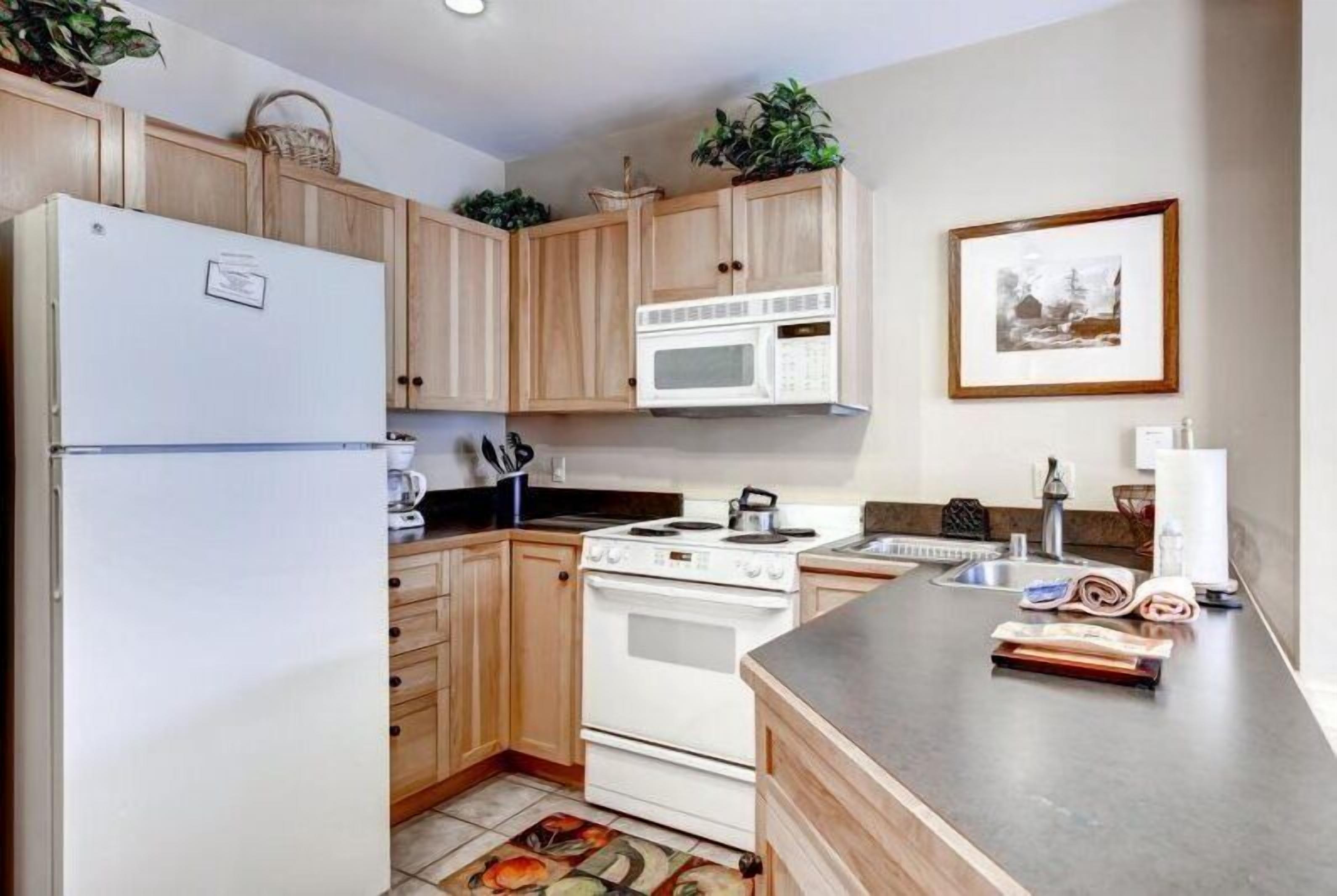 A kitchen with wooden cabinets, a white refrigerator, a microwave, a stove, and a sink.