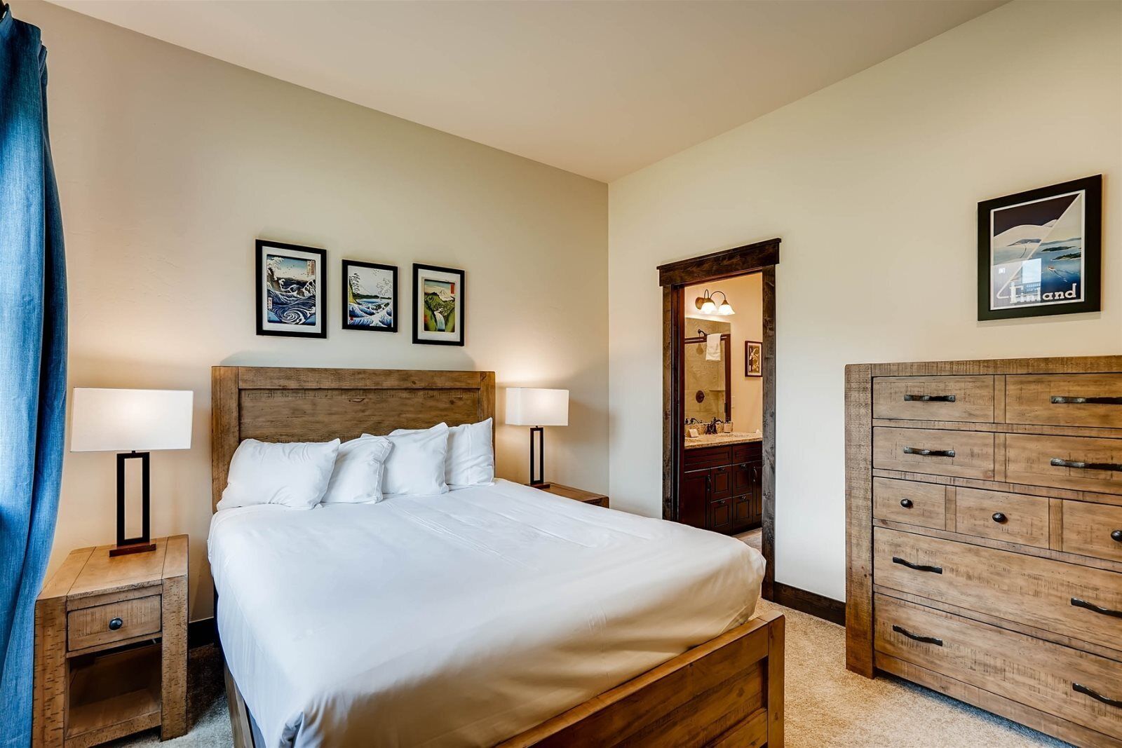 A neatly arranged bedroom with a wooden bed, bedside lamps, a dresser, and wall-mounted artwork.