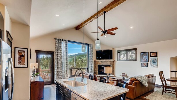 Uma cozinha espaçosa com uma ilha grande, uma sala de jantar com mesa de madeira e uma sala de estar com sofá e lareira.