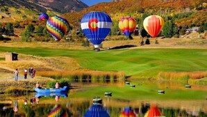 A golf course with hot air balloons in the background and a body of water in the foreground. - Snowmass Owl Creek 9904 (Snowmass Village)