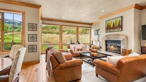 A spacious living room with leather sofas, a fireplace, and large windows offering a view of a golf course. - Snowmass Owl Creek 9904 (Snowmass Village)