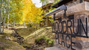 En skylt med texten ”WOODRUN PLACE” är fäst på en stenmur, omgiven av träd med gula löv, vilket signalerar en naturnära miljö.