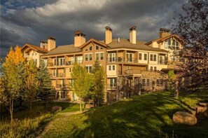 A multi-story building with a stone facade, multiple balconies, and a landscaped garden. - Snowmass Woodrun 9956 (Snowmass Village)