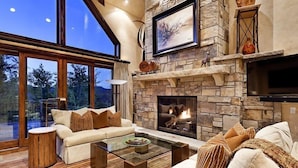 A spacious living room with a stone fireplace, large windows, and a cozy seating area. - Snowmass Castle Hill (Snowmass Village)