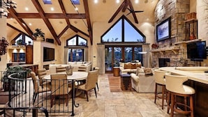A spacious living area with a high ceiling, stone fireplace, and large windows. - Snowmass Castle Hill (Snowmass Village)