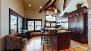 Una cocina amplia con armarios de madera, una isla central, taburetes de bar y ventanas grandes.