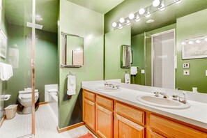 A bathroom with green walls, two sinks, wooden cabinets, a large mirror, and a glass shower enclosure.