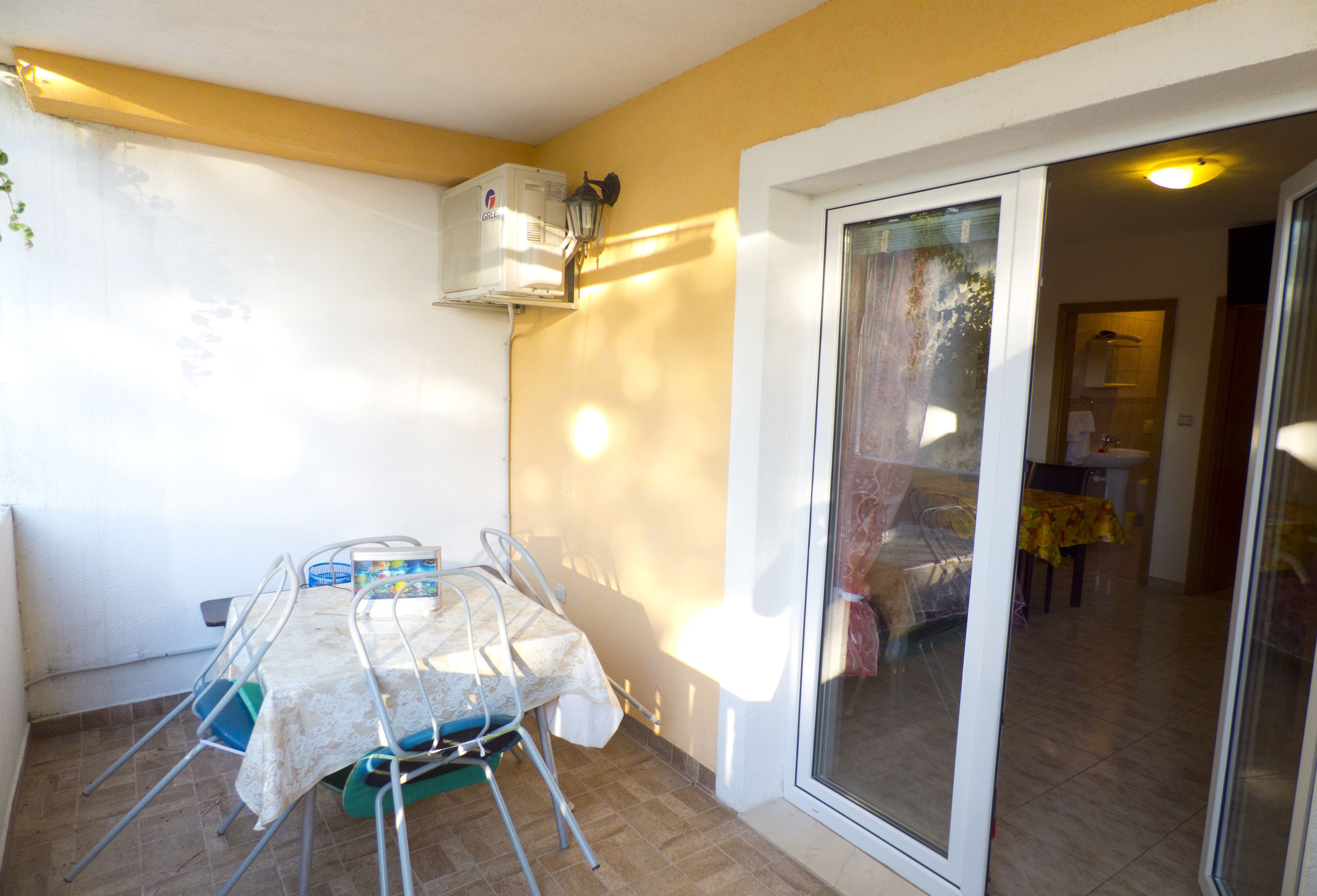 A balcony with a table and chairs, an air conditioning unit, and a sliding glass door leading to an interior room.