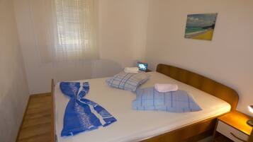 A neatly made bed with blue and white bedding, a bedside table with a lamp, and a painting of a beach on the wall.
