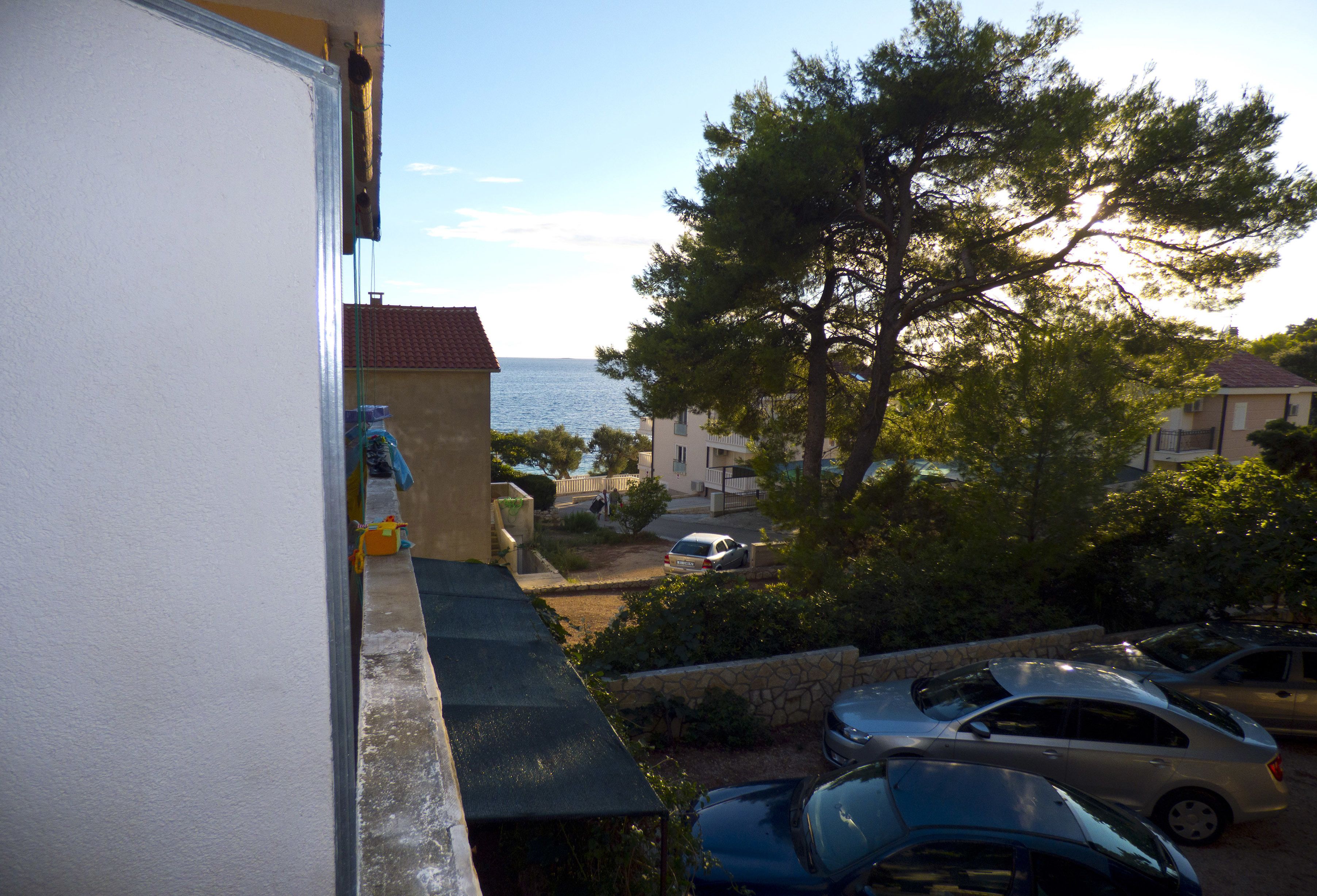 A residential area with a view of the sea, parked cars, and a stone wall.