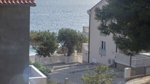 A coastal building with a view of the sea, a balcony, and a paved area with trees. - Apartments Plaza (Jelsa)