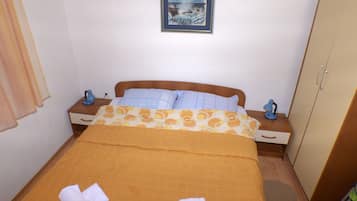 Uma cama bem arrumada com colcha estampada, duas mesas de cabeceira com abajures, um quadro na parede e um guarda-roupa.