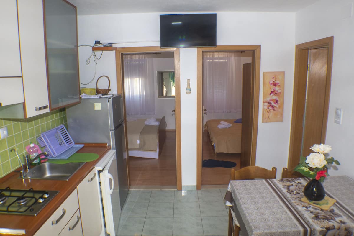 A compact kitchen with a refrigerator, stove, and sink. There is a dining area with a table and chairs, and a bedroom with a bed and a window.
