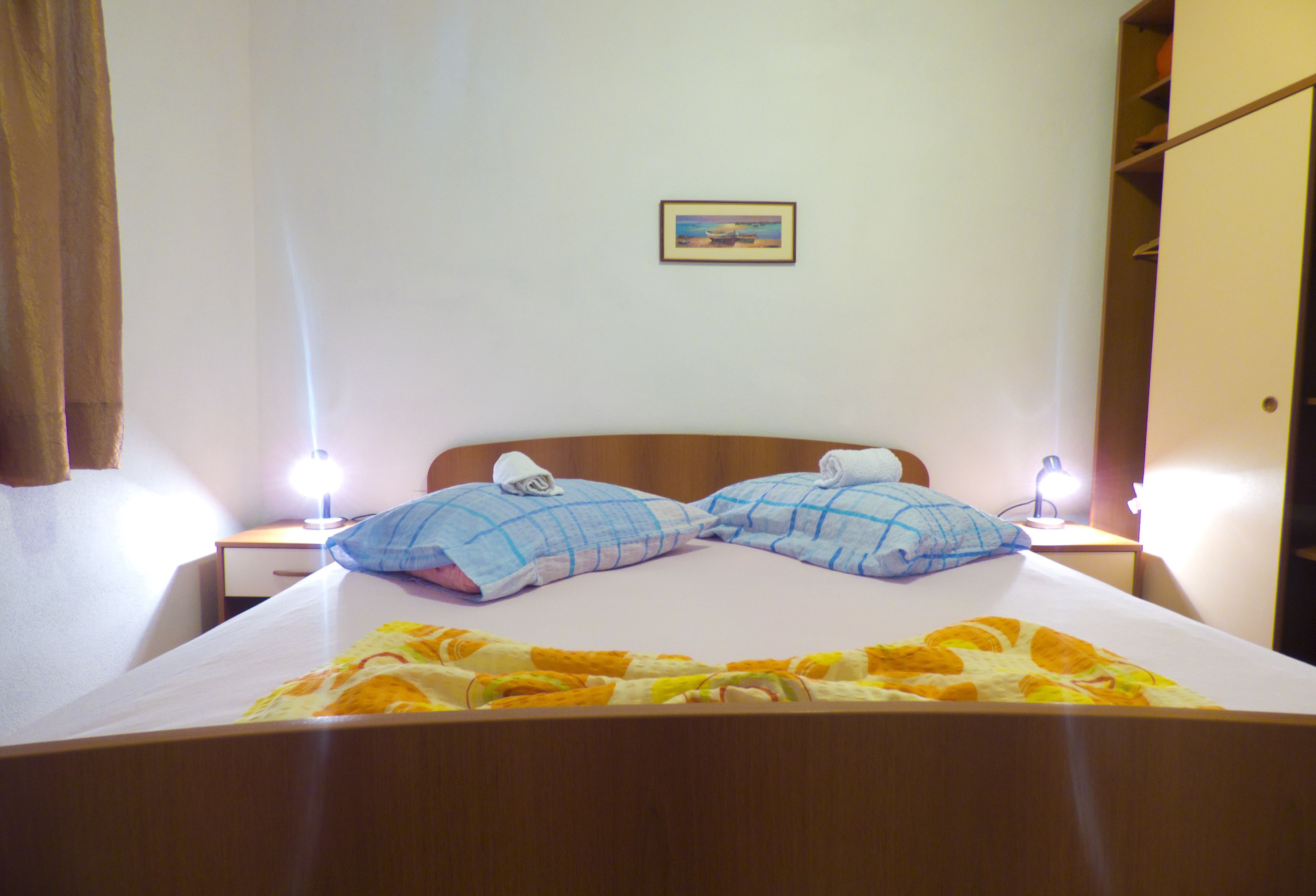 Ein ordentlich gemachtes Bett mit floralem Überwurf, zwei Kissen und zwei Nachttischlampen.
