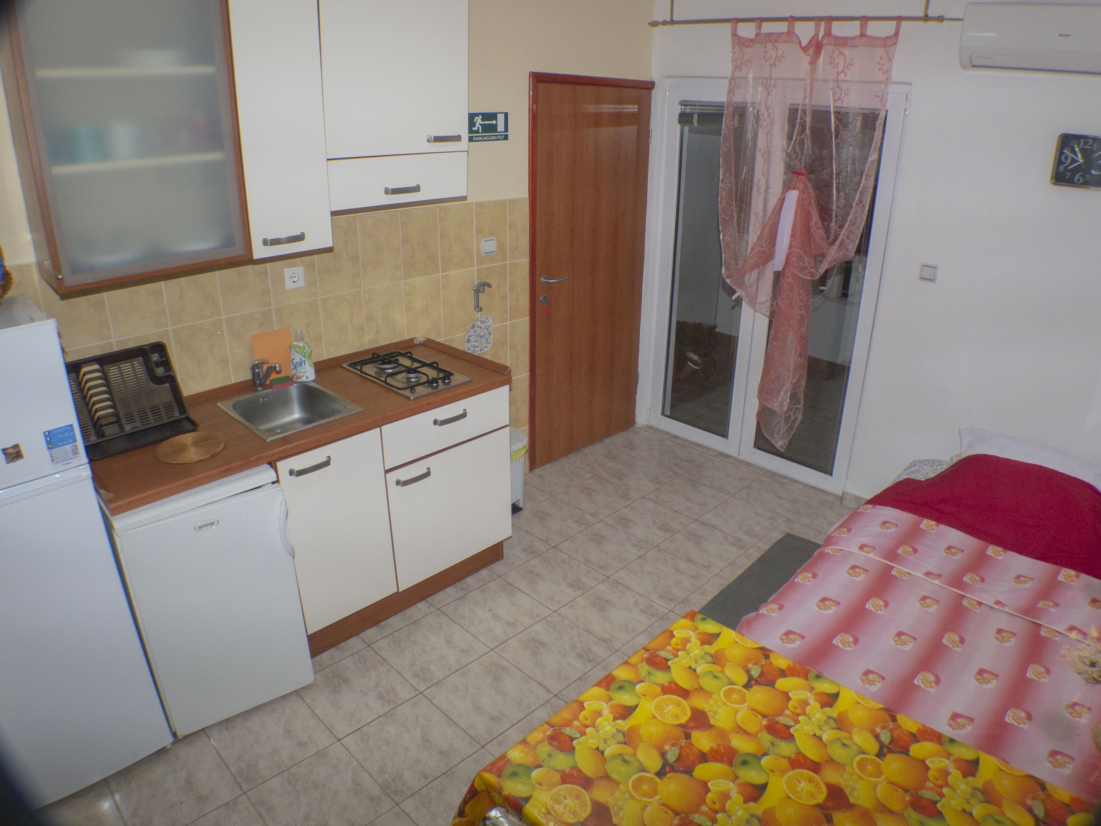Een compacte keuken met een spoelbak, fornuis en kasten, een kleine koelkast, en een schuifpui naar een balkon.