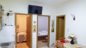 A compact hotel room with a kitchenette, a bed, a dining area with a table and chairs, and a TV mounted on the wall. - Apartments Plaza (Jelsa)