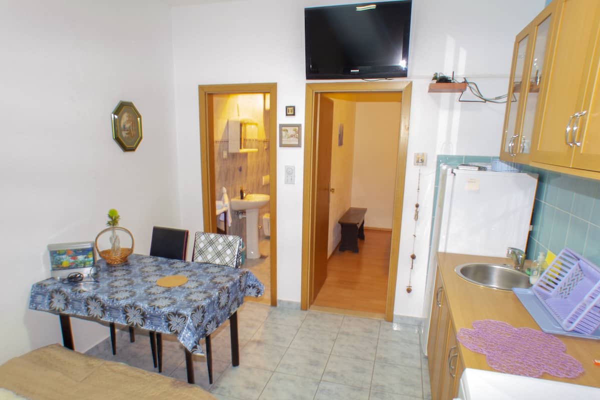 A compact kitchen with a dining area, a television mounted above the counter, and a small bench in the adjacent room.