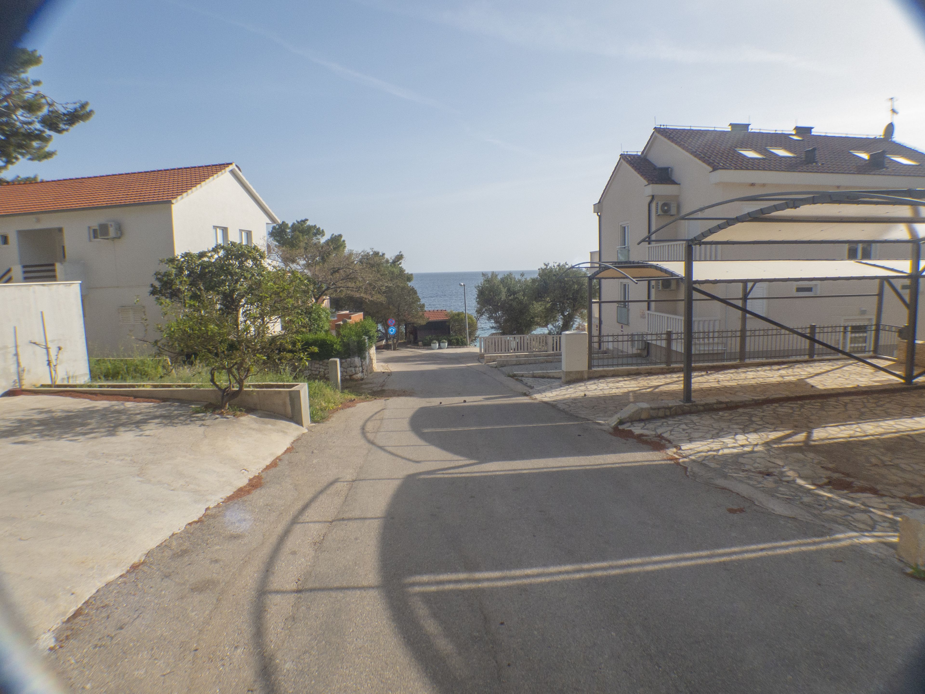 Una tranquila calle residencial con casas, cielo despejado y vista al mar.