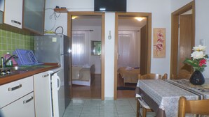 A compact kitchen with a refrigerator, a sink, and a dining area with a table and chairs. - Apartments Plaza (Jelsa)