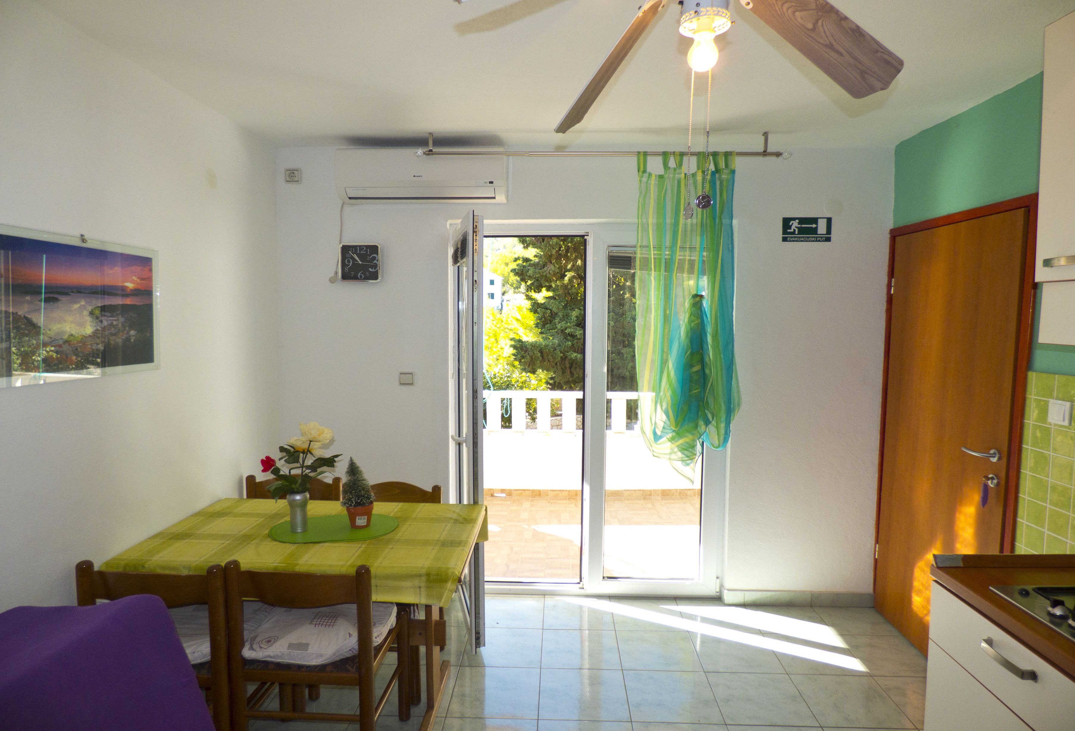 Zona de menjador amb taula i cadires, un ventilador de sostre i vista a una zona exterior a través d'una porta de vidre.
