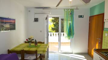 Zona de menjador amb taula i cadires, un ventilador de sostre i vista a una zona exterior a través d'una porta de vidre.