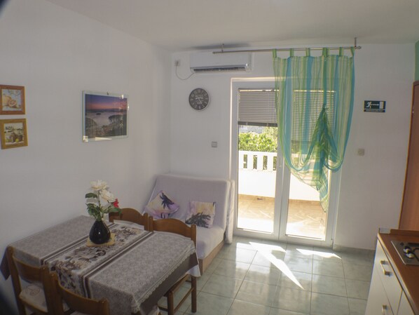 A dining area with a table set for two, a sofa, and a view of the outside. - Apartments Plaza (Jelsa)