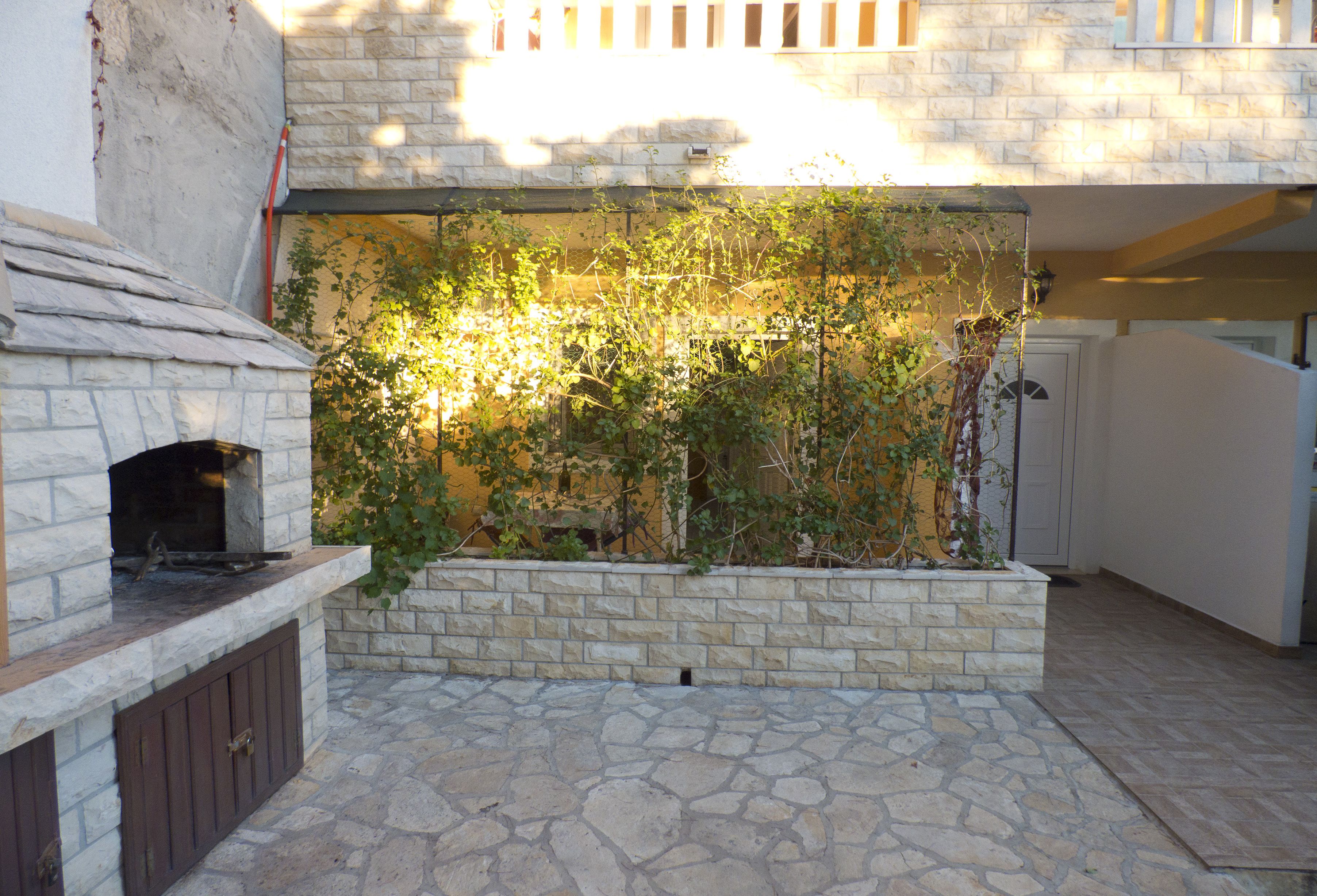 An outdoor patio with a stone fireplace, a stone wall with climbing plants, and a door leading to a covered area.
