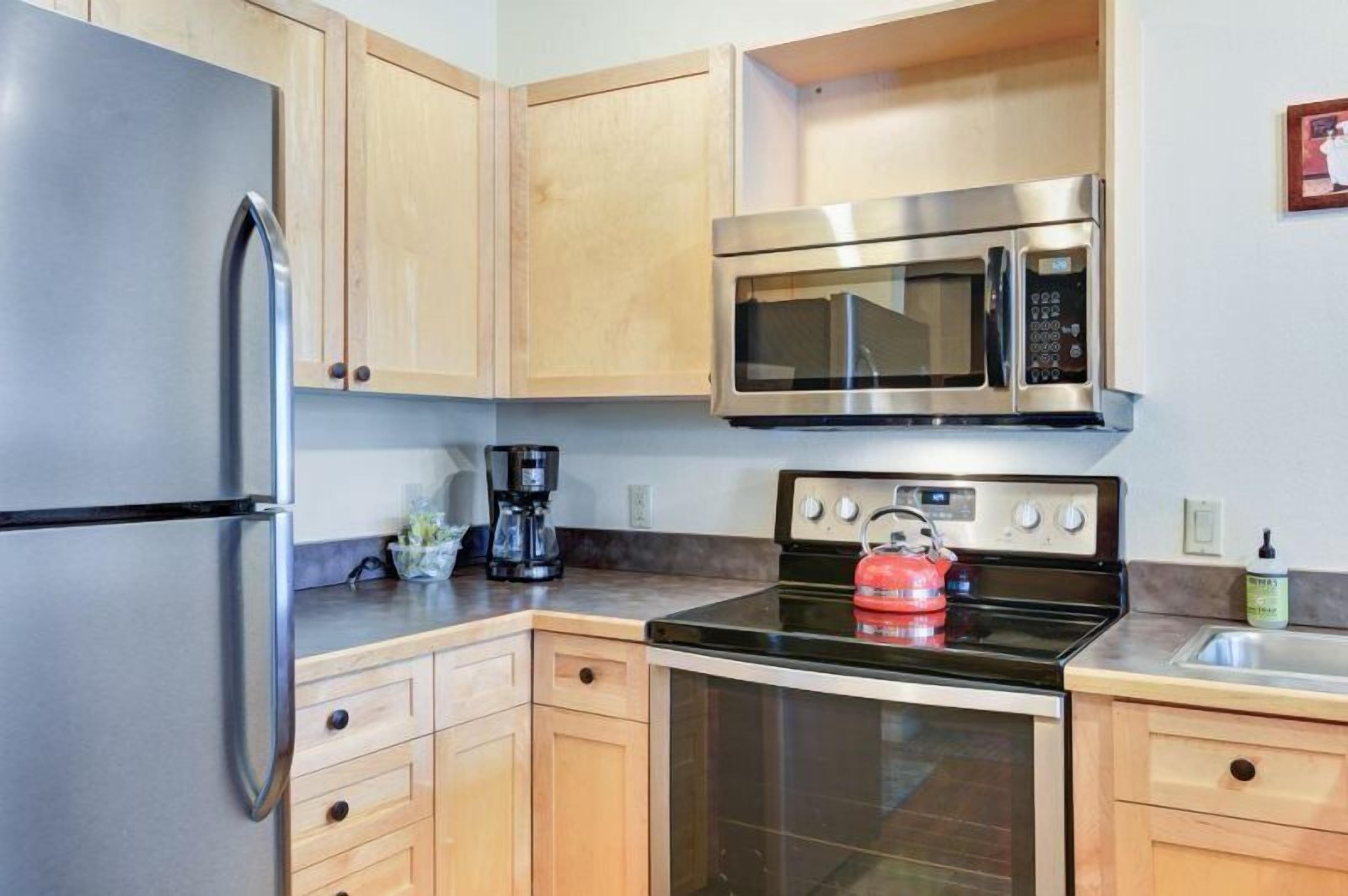 A kitchen with stainless steel appliances, wooden cabinets, and a black stove.